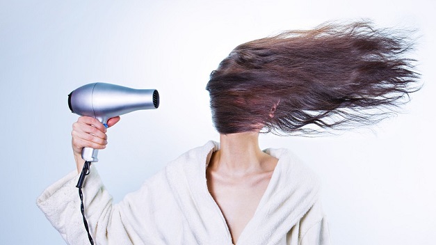 Frau föhnt sich die Haare ins Gesicht.