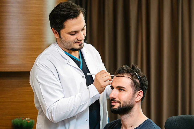 Dr. Balwi zeichnet bei Patienten die Haarlinie ein