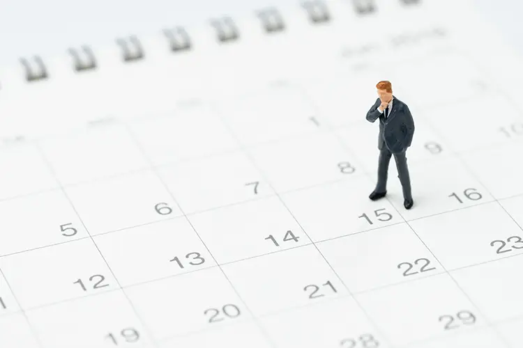 Eine Figur eines Mannes, die auf einem Kalender steht und nachdenklich auf den Kalender schaut
