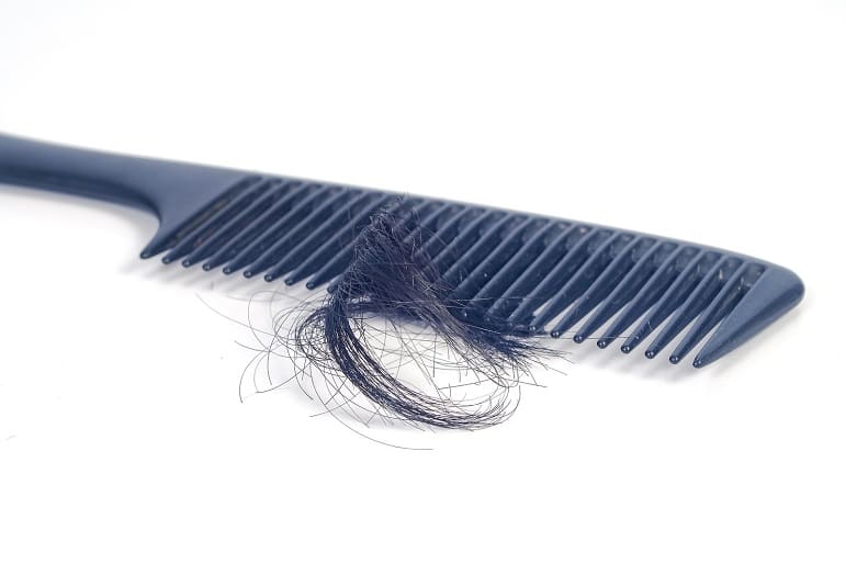 Eine Haartransplantation kann bei Haarverlust Abhilfe schaffen Ein schwarzer Kamm liegt neben einem Büschel Haare