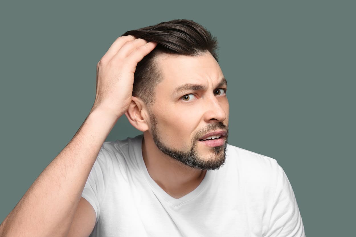 Junger Mann checkt frühzeitigen Haarausfall im Spiegel