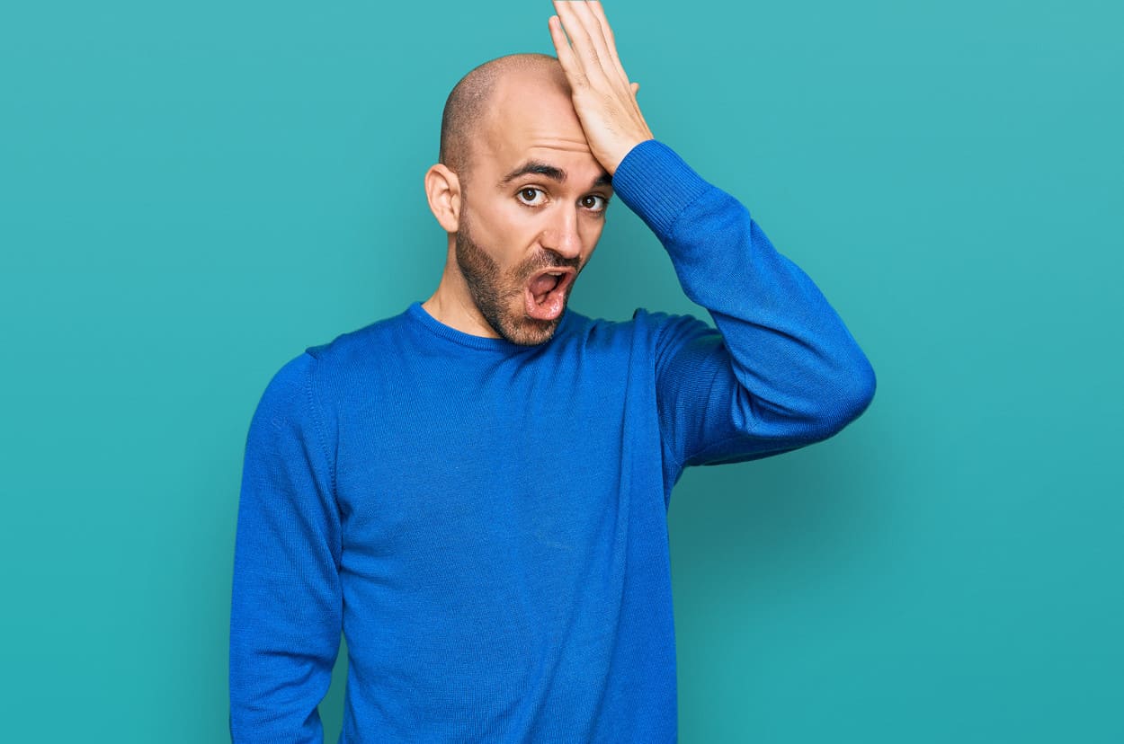 Mann mit Glatze fasst sich an den Kopf.