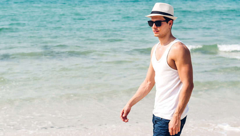 Mann läuft am Strand mit Hut.