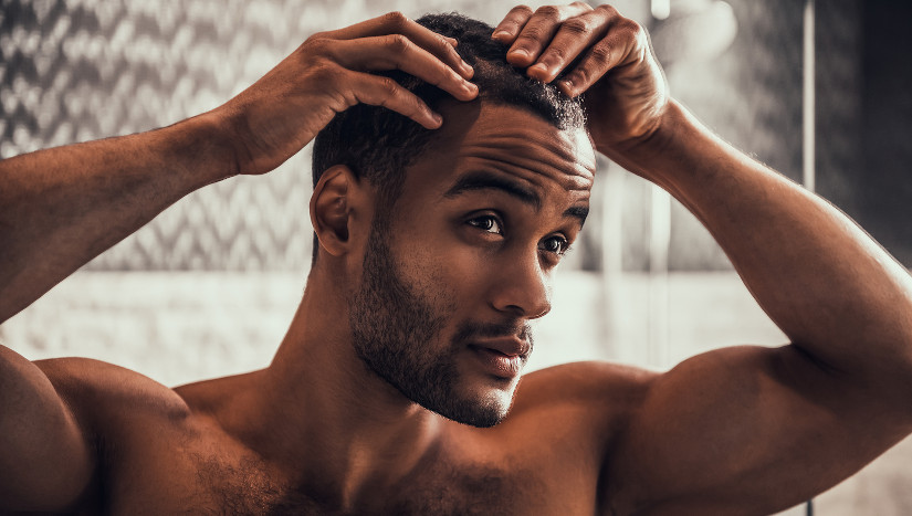 Mann betrachtet seinen Haarausfall im Spiegel.