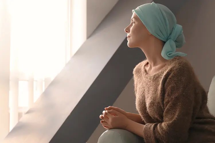 Krebspatientin mit Kopftuch blickt nachdenklich aus dem Fenster – symbolisiert Hoffnung, emotionale Stärke und den Umgang mit Haarverlust während der Therapie