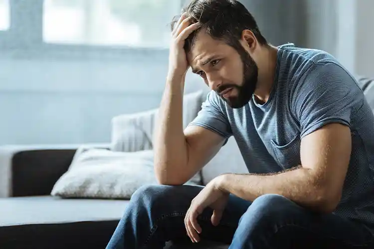 Ein Mann sieht deprimiert aus, mit der Hand am Kopf und ist sichtbar traurig