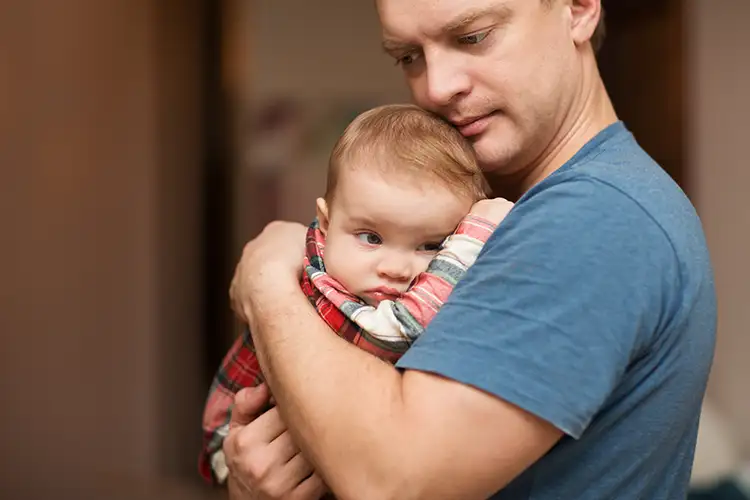 Ein Mann hält sein Baby im Arm und blickt besorgt.