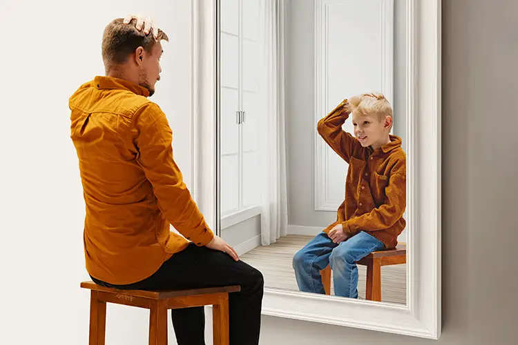 Ein Mann blickt in den Spiegel – im Spiegelbild erkennt er sich als Kind. Symbolisiert die Sehnsucht nach dem früheren Ich und den Wunsch nach Wiederherstellung.