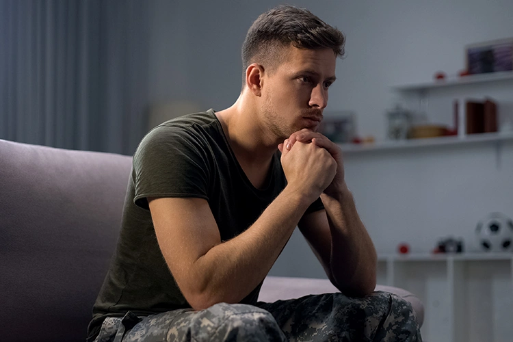 Ein Mann sitzt nachdenklich auf der Couch, stützt den Kopf auf die Hände und blickt traurig vor sich hin – Sinnbild für innere Leere, Depression oder die seelische Belastung