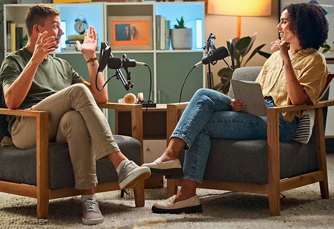 Zwei Personen sitzen in Sesseln und unterhalten sich vor Mikrofonen