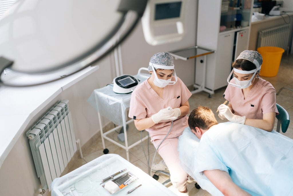 Zwei Ärztinnen in OP-Kleidung führen bei einem Patienten eine Haartransplantation durch