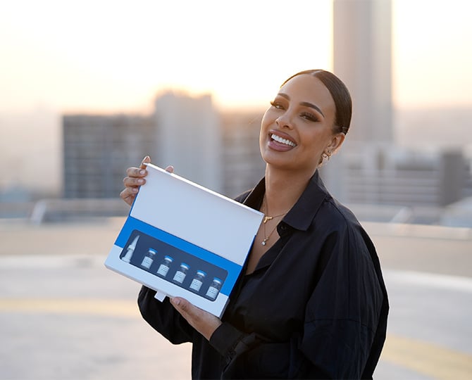 Frau lacht und hält eine Dr.Balwi Produktbox mit mehreren Fläschchen in die Kamera