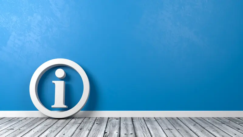 Weißes Informationssymbol mit einem Kreis vor blauer Wand und Holzboden
