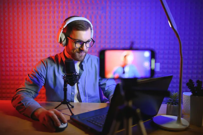 Junger Mann mit Kopfhörern und Mikrofon am Laptop im Studio