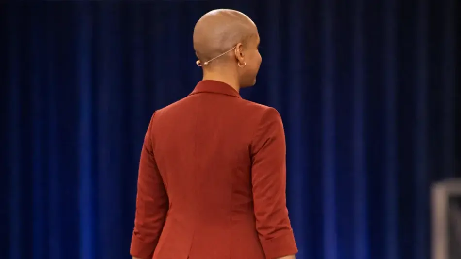 Bild zeigt eine Frau mit Glatze von hinten in einem terracotta farbenen Anzug