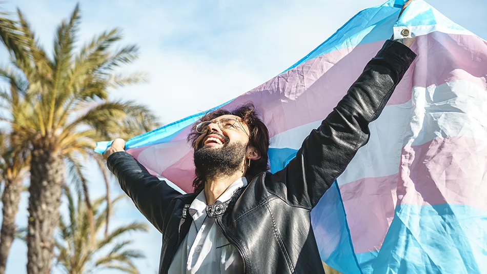 Person hält die Transgender-Flagge in die Höhe und lacht zufrieden