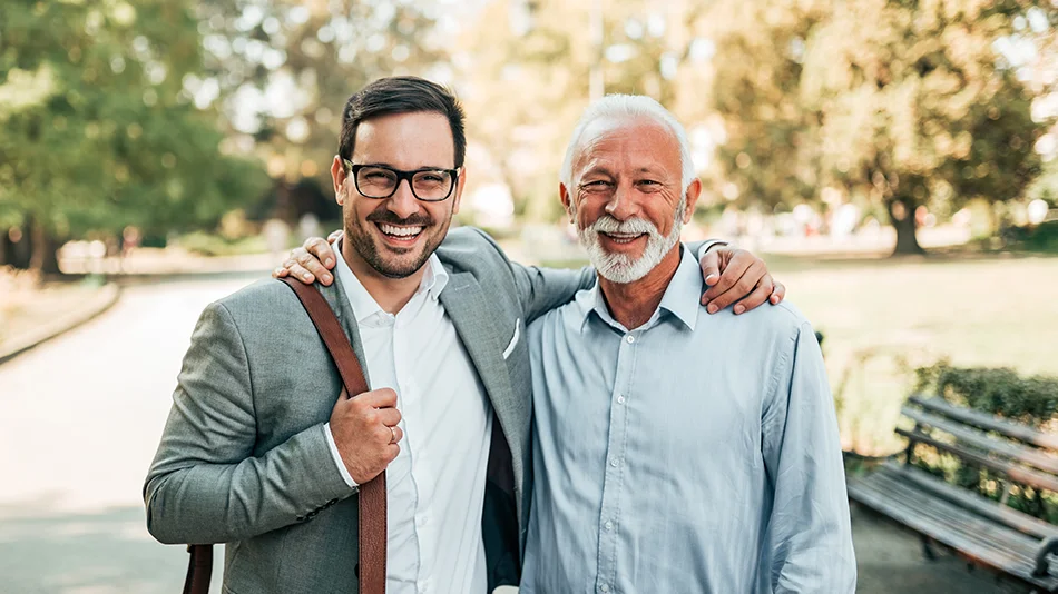 Junger und älterer Mann stehen lächelnd nebeneinander im Park
